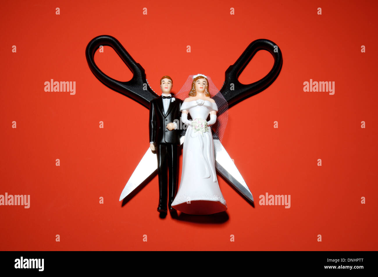 Plastic miniature wedding figures with scissors on a red background. Stock Photo