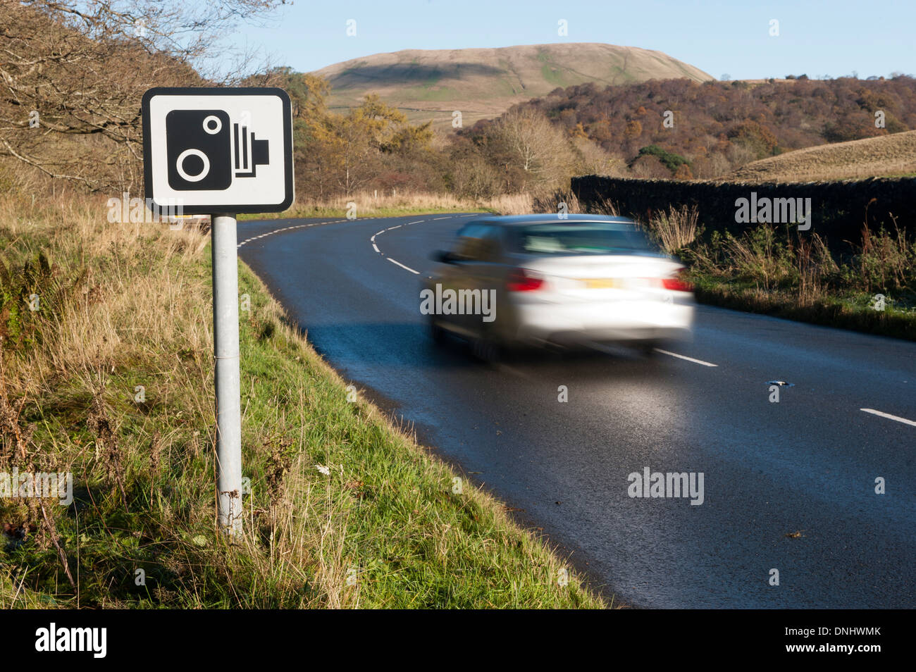 Car on rural road going past a speed camera warning sign. Cumbria, UK Stock Photo