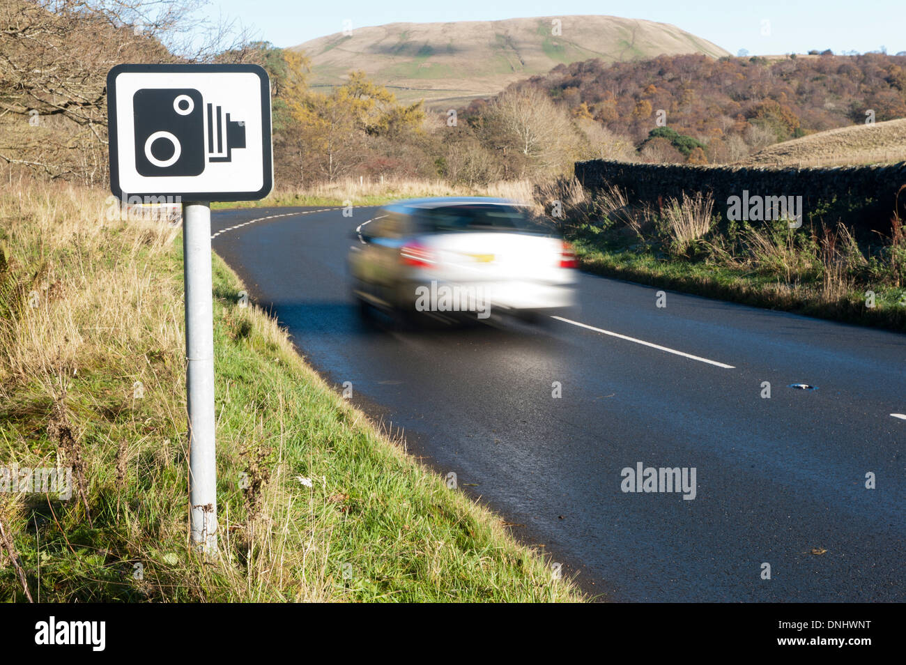 Car on rural road going past a speed camera warning sign. Cumbria, UK Stock Photo