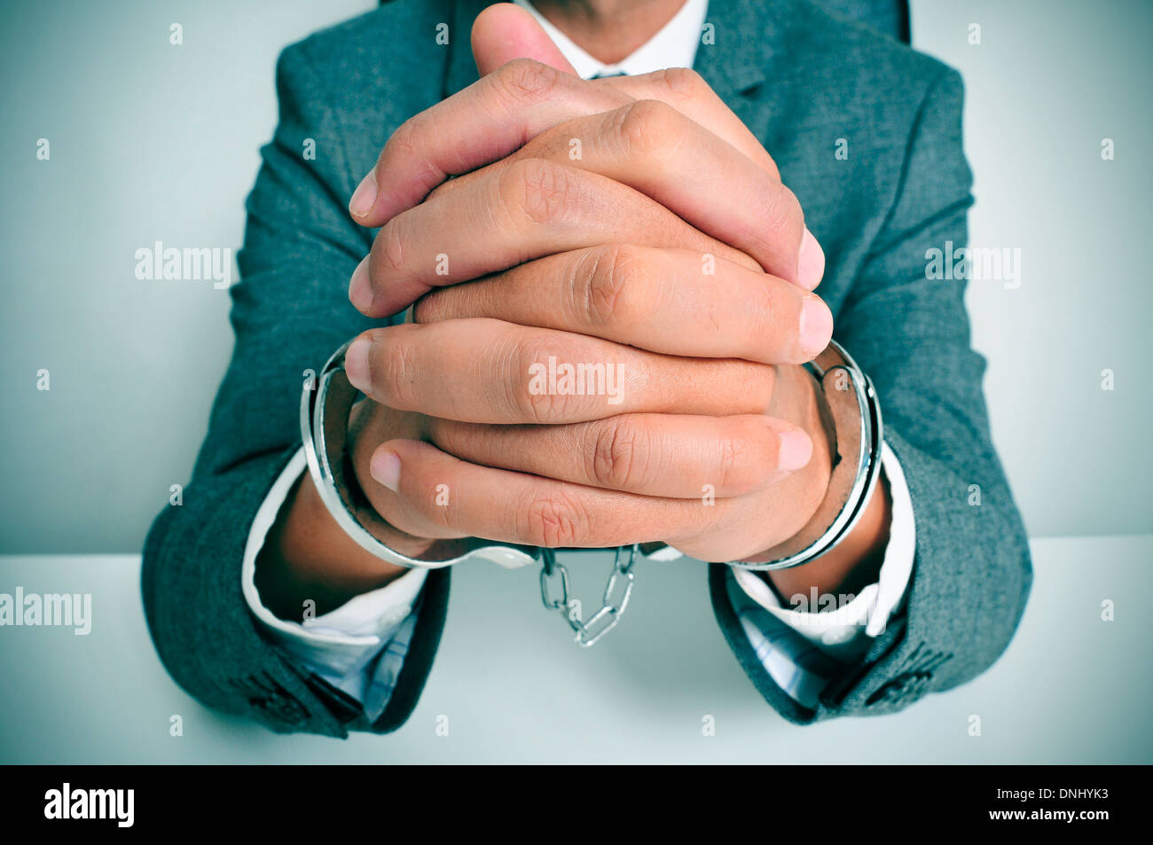 a man wearing a suit sitting in a desk, with handcuffs in his wrists Stock Photo