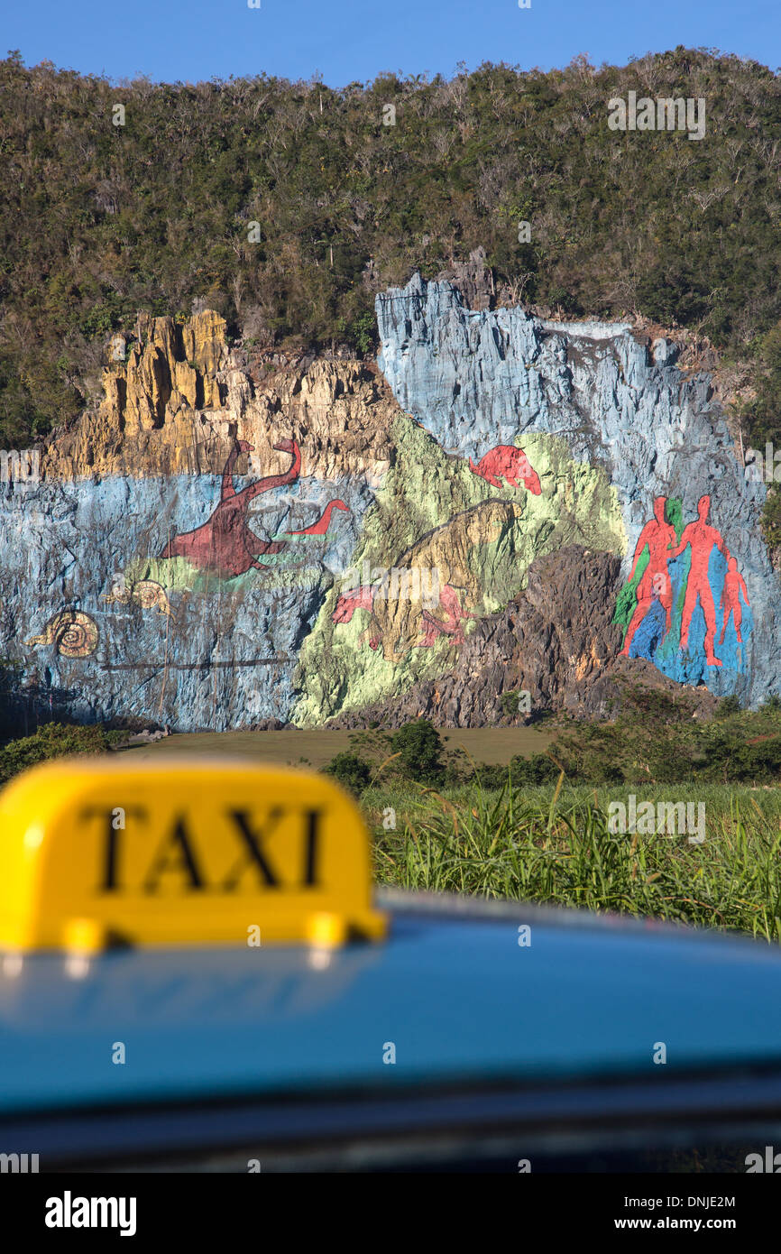 TAXI IN FRONT OF THE MURAL OF EVOLUTION, PREHISTORIC WALL (MURAL DE LA PREHISTORIA) COMMISSIONED BY FIDEL CASTRO IN 1961, PAINTING ON A SLOPE OF A MOGOTE (MOUNTAINOUS LIMESTONE HILLOCK), VINALES VALLEY, LISTED AS A WORLD HERITAGE SITE BY UNESCO, CUBA, THE Stock Photo