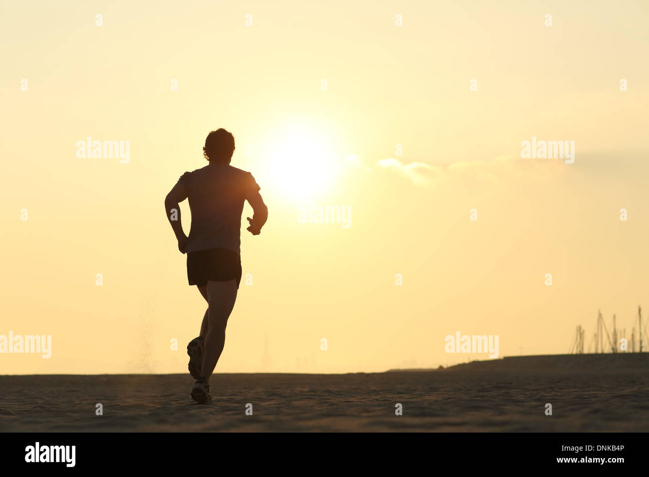 Backlight of a jogger running on the beach with the sun beside Stock Photo
