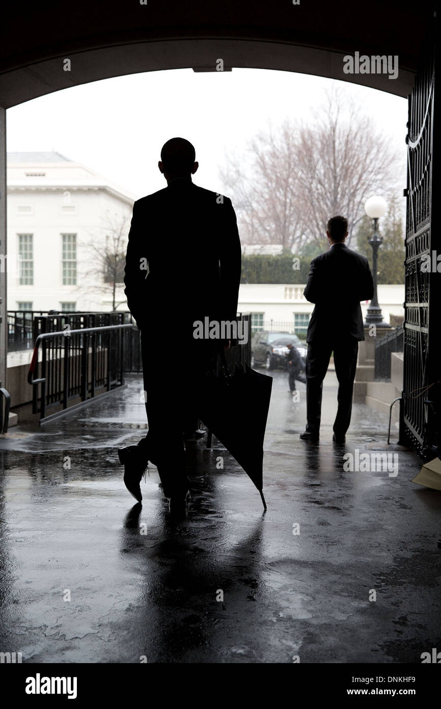 US President Barack Obama leans on an umbrella as he waits for heavy rain to let up before crossing from the Eisenhower Executive Office Building to the West Wing of the White House March 12, 2013 in Washington, DC. Most of the staff and Secret Service with the President didn't have umbrellas so he waited for the rain to subside before crossing. Stock Photo