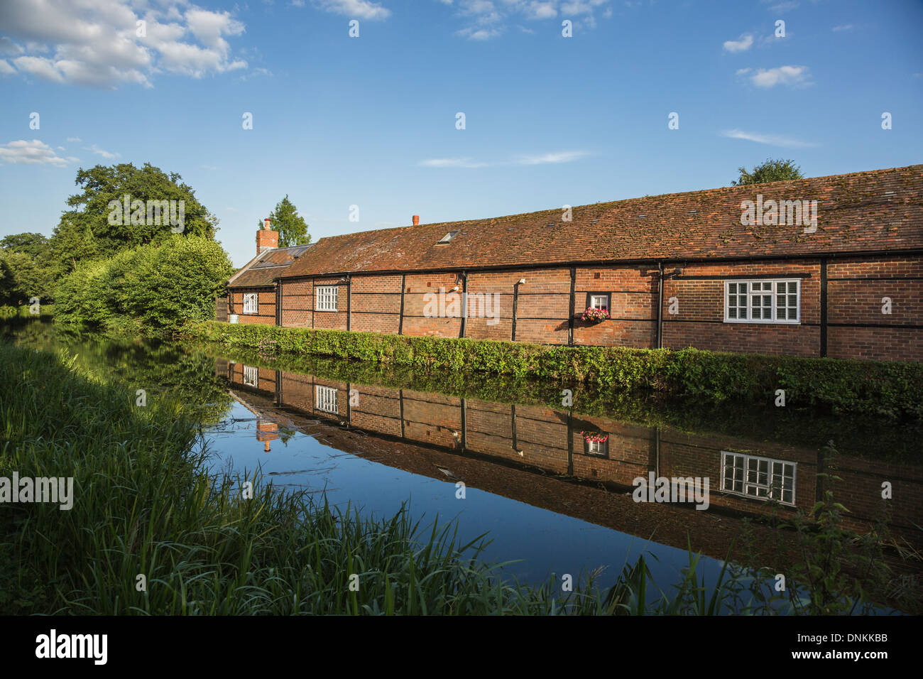Timbered brick building on River Wey at Pyrford, Surrey, UK in summer with reflection in still water Stock Photo