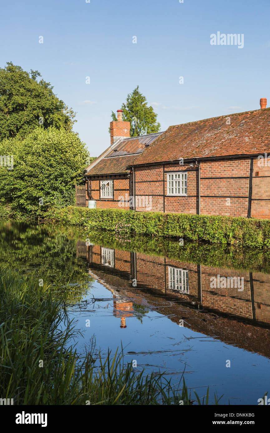 Timbered brick building on River Wey at Pyrford, Surrey, UK in summer with reflection in still water Stock Photo