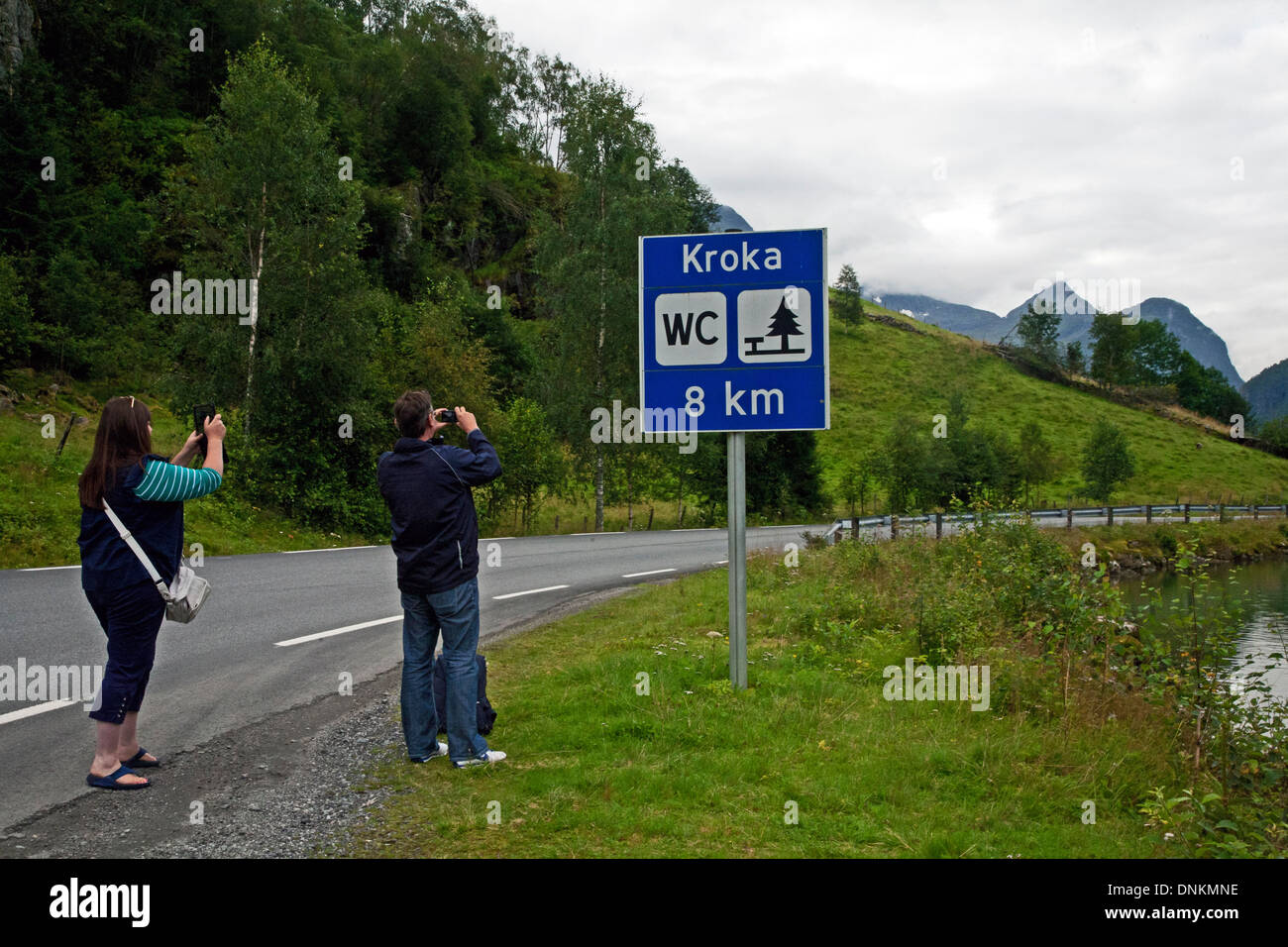 Couple taking pictures of signpost with mobile phones in the village of Geiranger, Norway, Europe Stock Photo