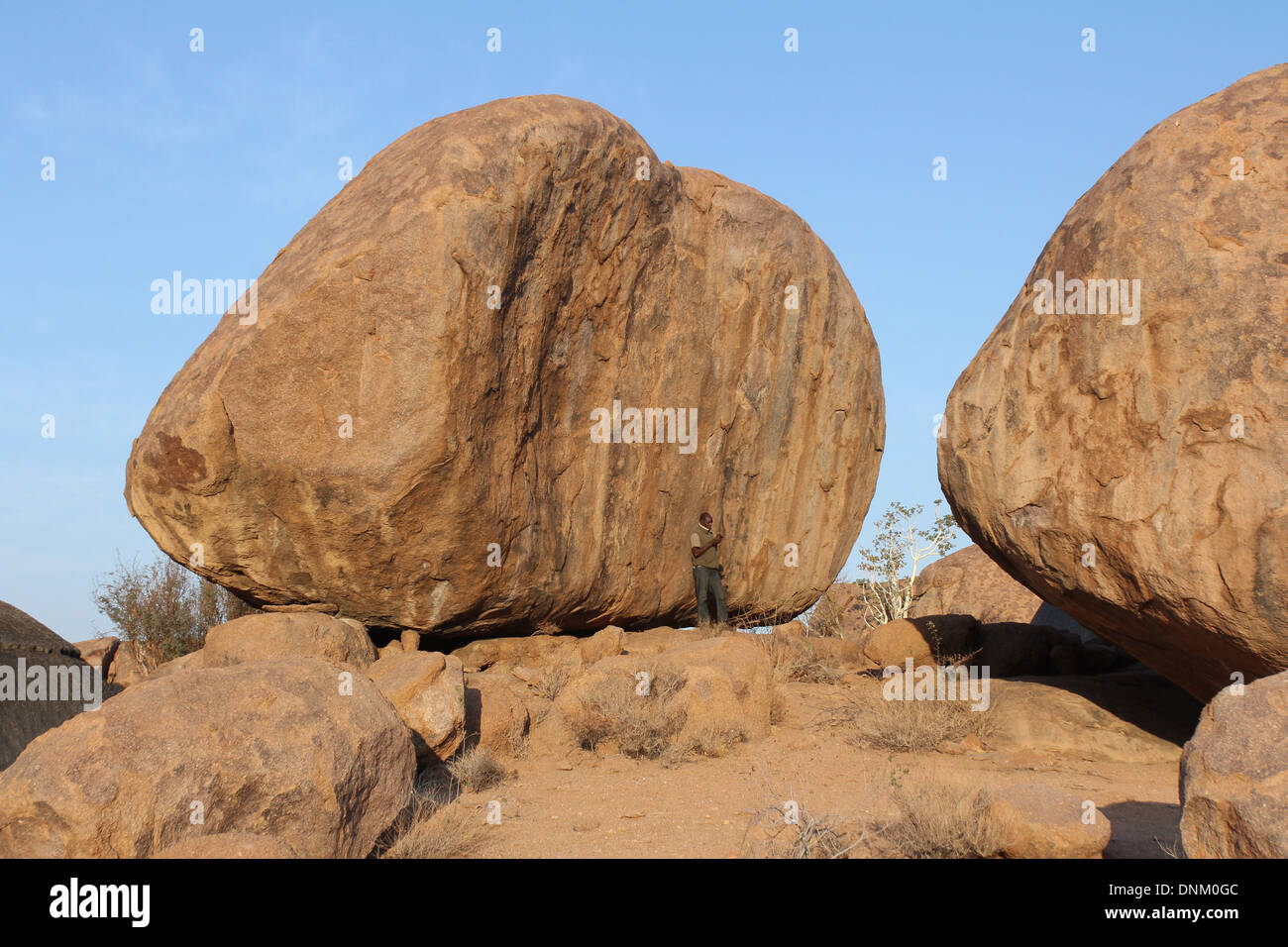 Man standing against a  giant boulder in the Namib Desert,Namibia. Stock Photo