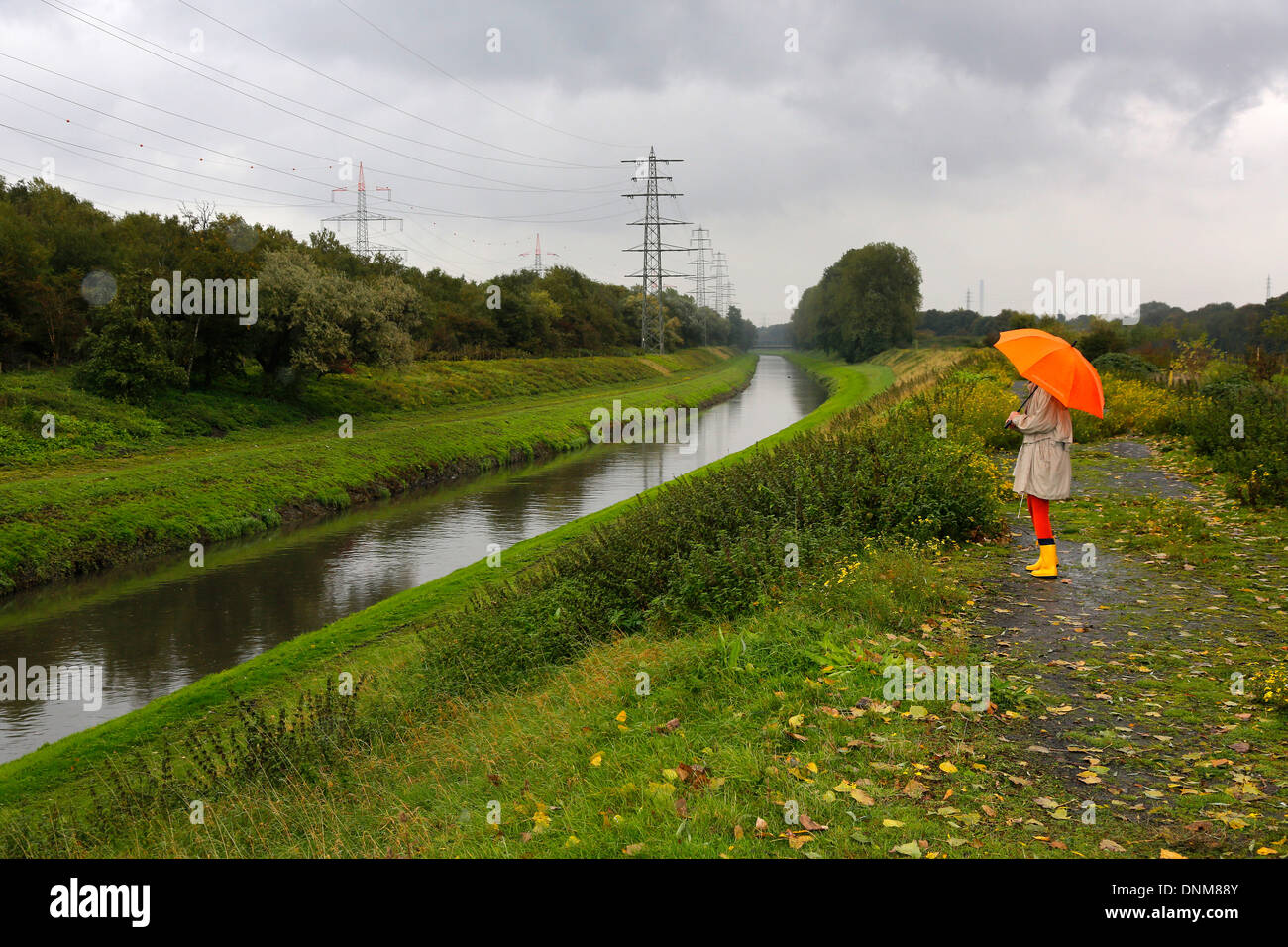 Oberhausen, Germany, a young woman walks in the rain with umbrella walking along the Emscher Stock Photo