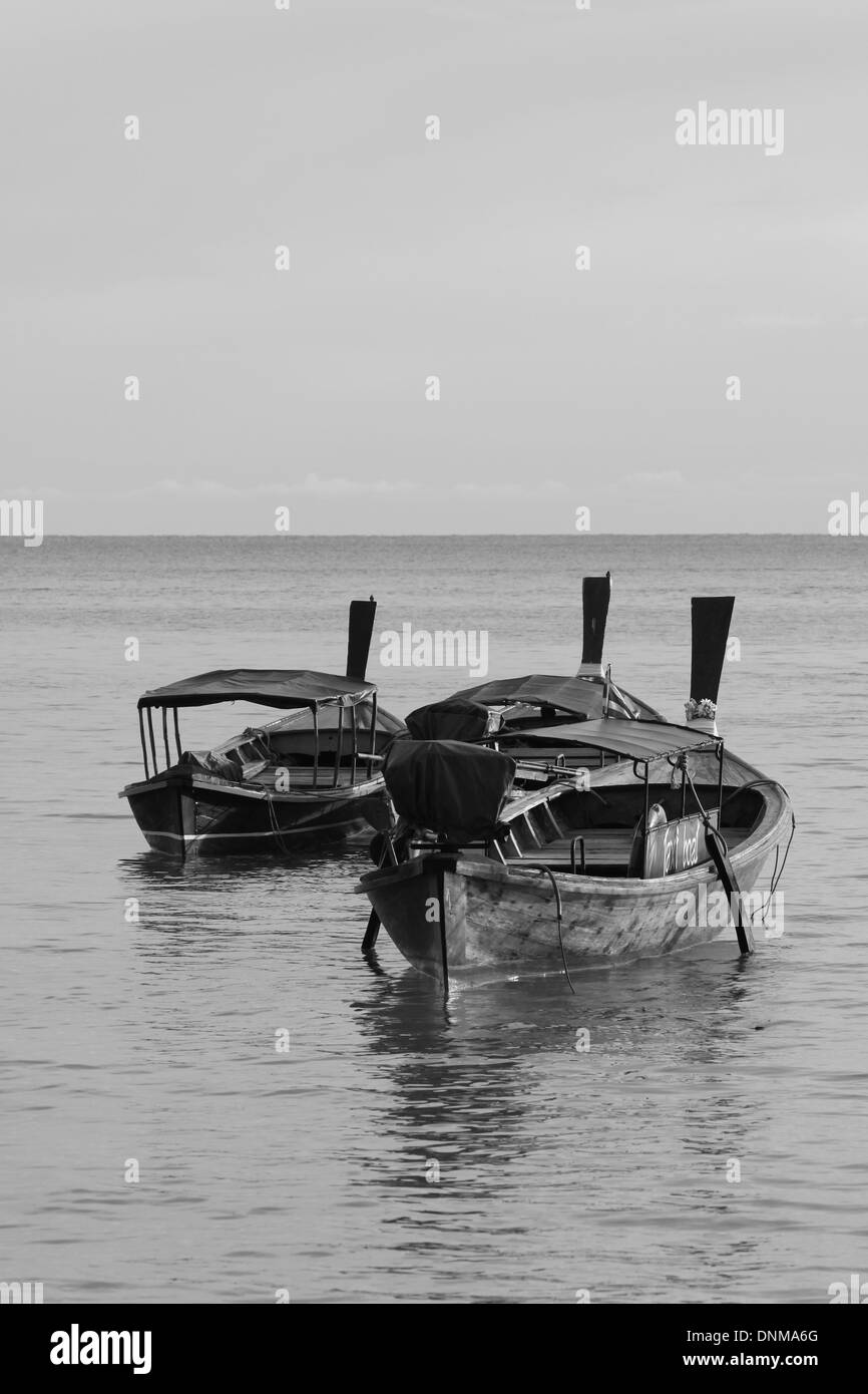 A black and white photograph of some longtail boats in Thailand against a backdrop of a calm sea and horizon. Stock Photo