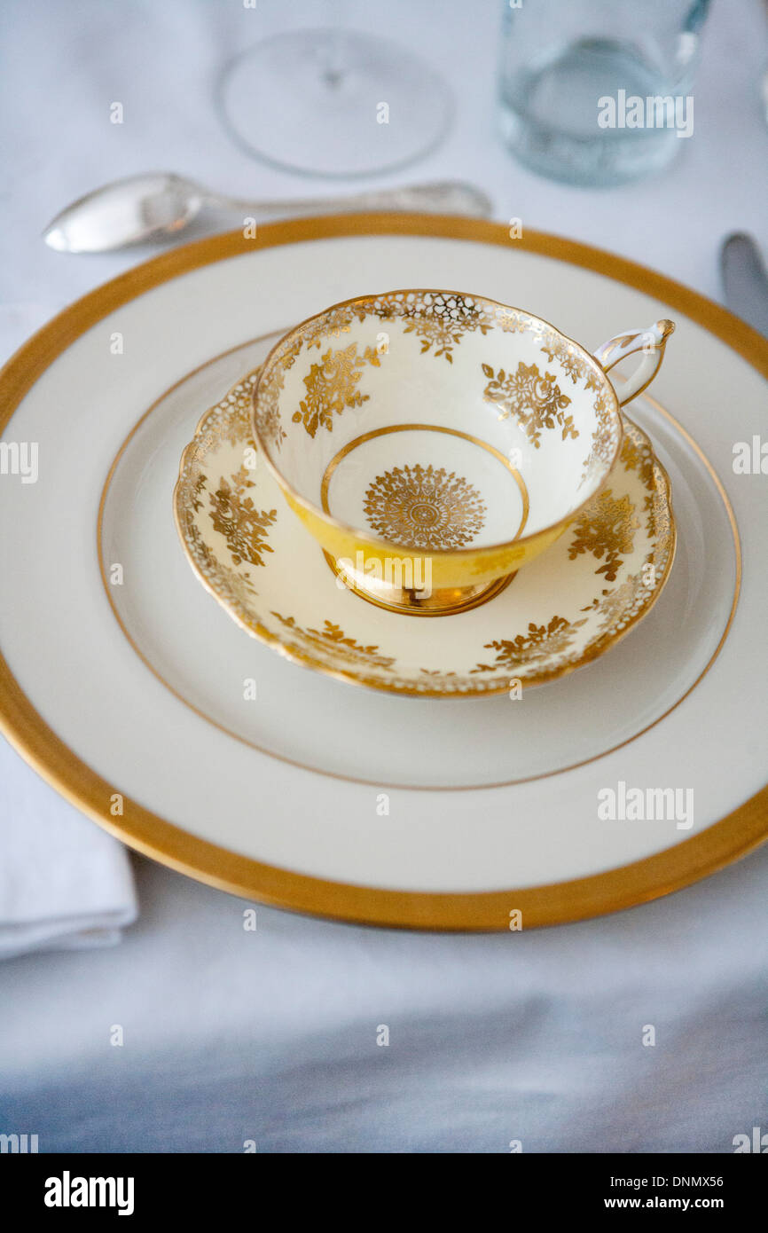 Formal Dining Table Setting with Gold-Accented Teacup and Saucer on Plate with Silverware Stock Photo