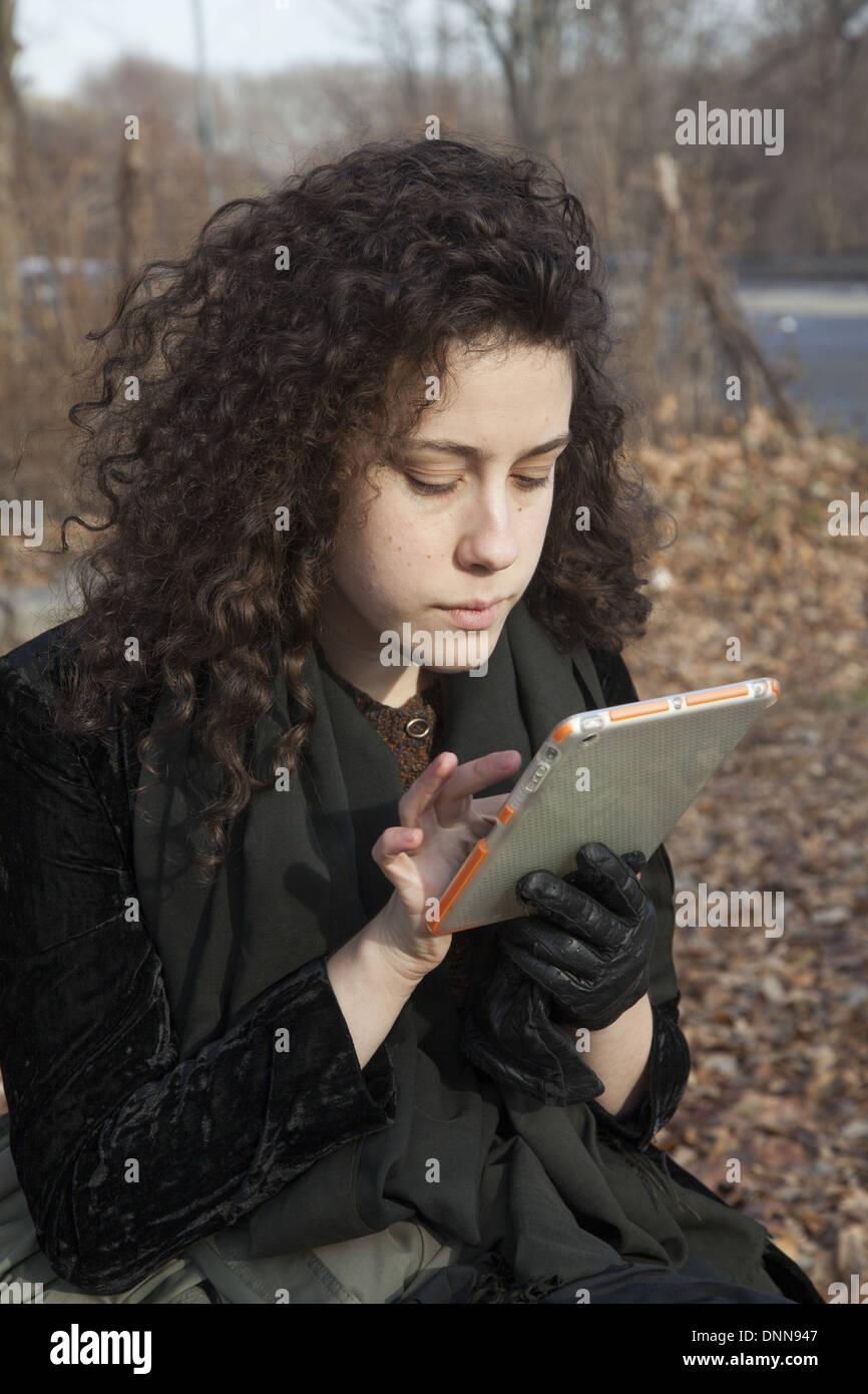 Young woman uses her ipad mini tablet, sitting in the park in Brooklyn, NY. Stock Photo