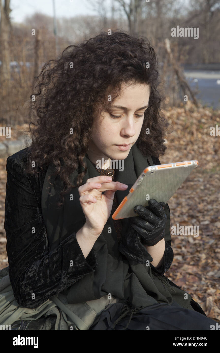 Young woman uses her ipad mini tablet, sitting in the park in Brooklyn, NY. Stock Photo