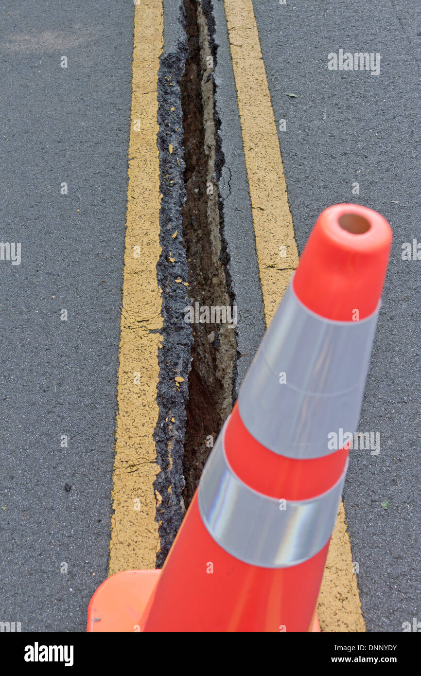 Close up of an orange cone with a large asphalt crack in the road behind it Stock Photo