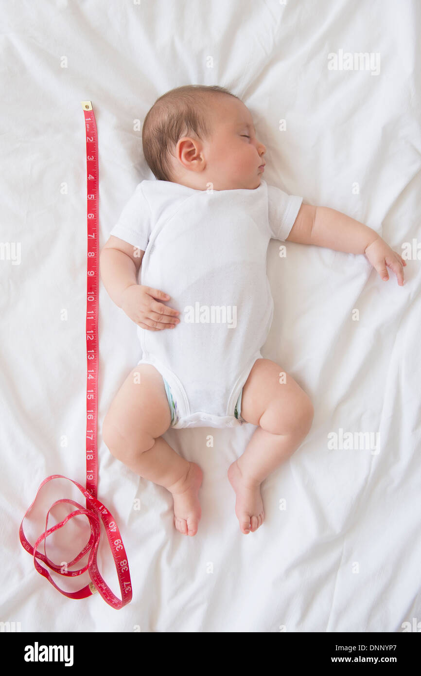 Baby girl (25 months) sleeping in bed with tape measure Stock Photo