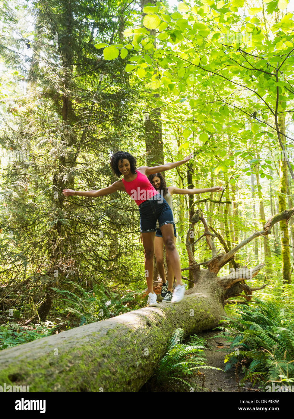 USA, Oregon, Portland, Two young women walking on log in forest Stock Photo
