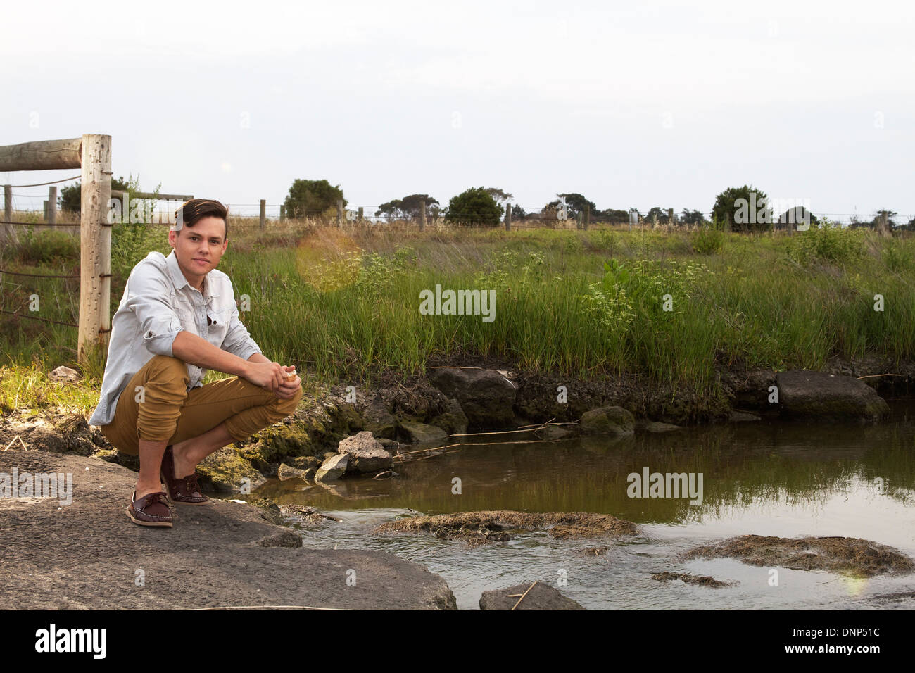 young man squatting by water in country side Stock Photo