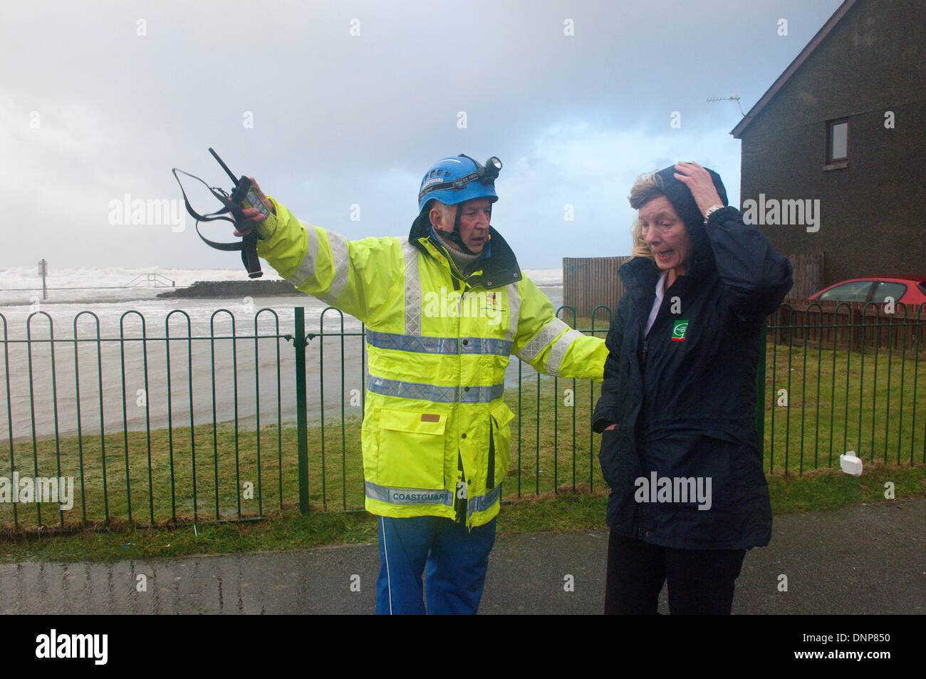 Barmouth, Gwynedd, Wales, UK. 3rd January 2014. Anne Lewis, a community carer, whose property is threatened by the sea which has breached the sea wall, is advised by a first responder. With over 500 flood warnings and alerts nationwide The Environment Agency has warned people to be prepared to protect themselves and their homes and to stay well back from high water mark on coastlines. Credit:  Graham M. Lawrence/Alamy Live News. Stock Photo