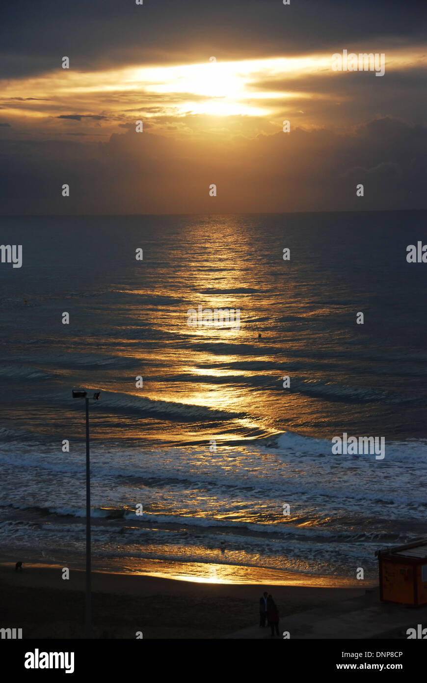 Sun peeping through clouds, while setting over the Mediterranean Coast of Sitges, Spain Stock Photo