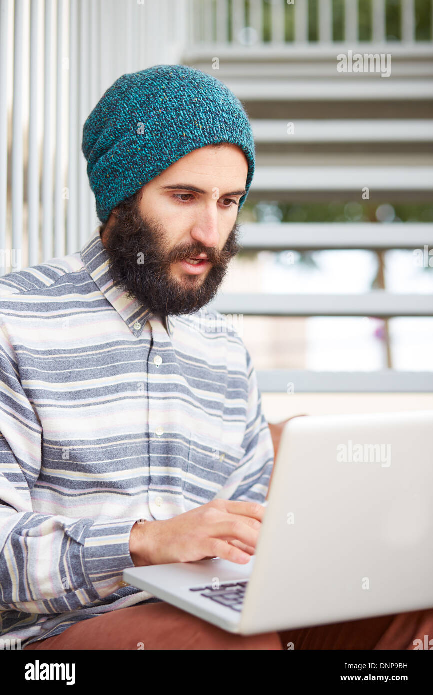 Young bearded hipster student using computer at university campus Stock Photo