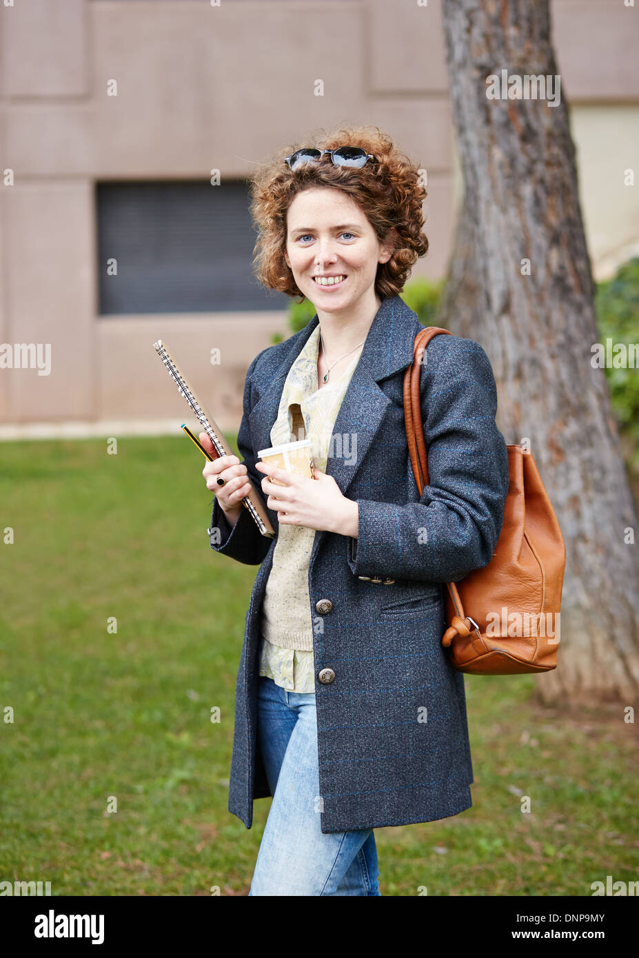 Female redhead student carrying notebook and coffee to go at university campus Stock Photo
