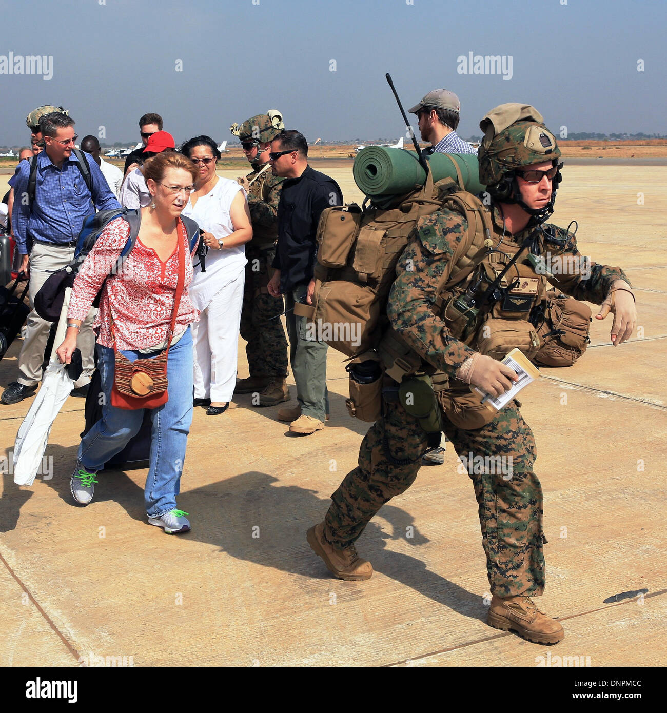 A US Marine from the Crisis Response team guides American citizens to an evacuation flight January 3, 2014 in Juba, South Sudan. The Marines evacuated more than 20 personnel from the U.S. Embassy as conflict escalates in South Sudan following a failed coup attempt. Stock Photo