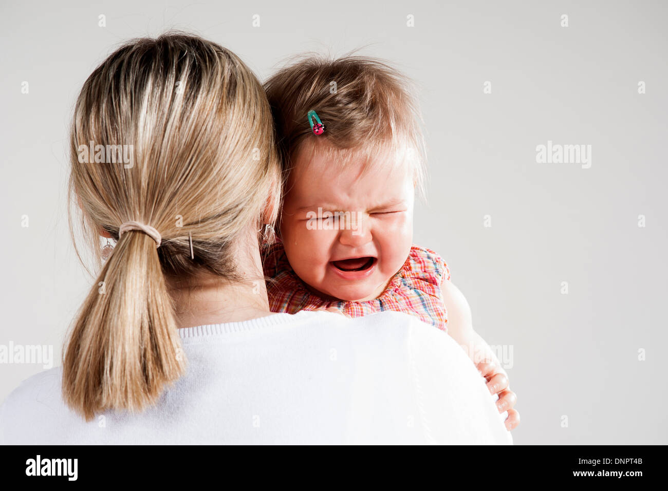 Over the Shoulder View of Mother holding Crying Baby Girl, Studio Shot Stock Photo