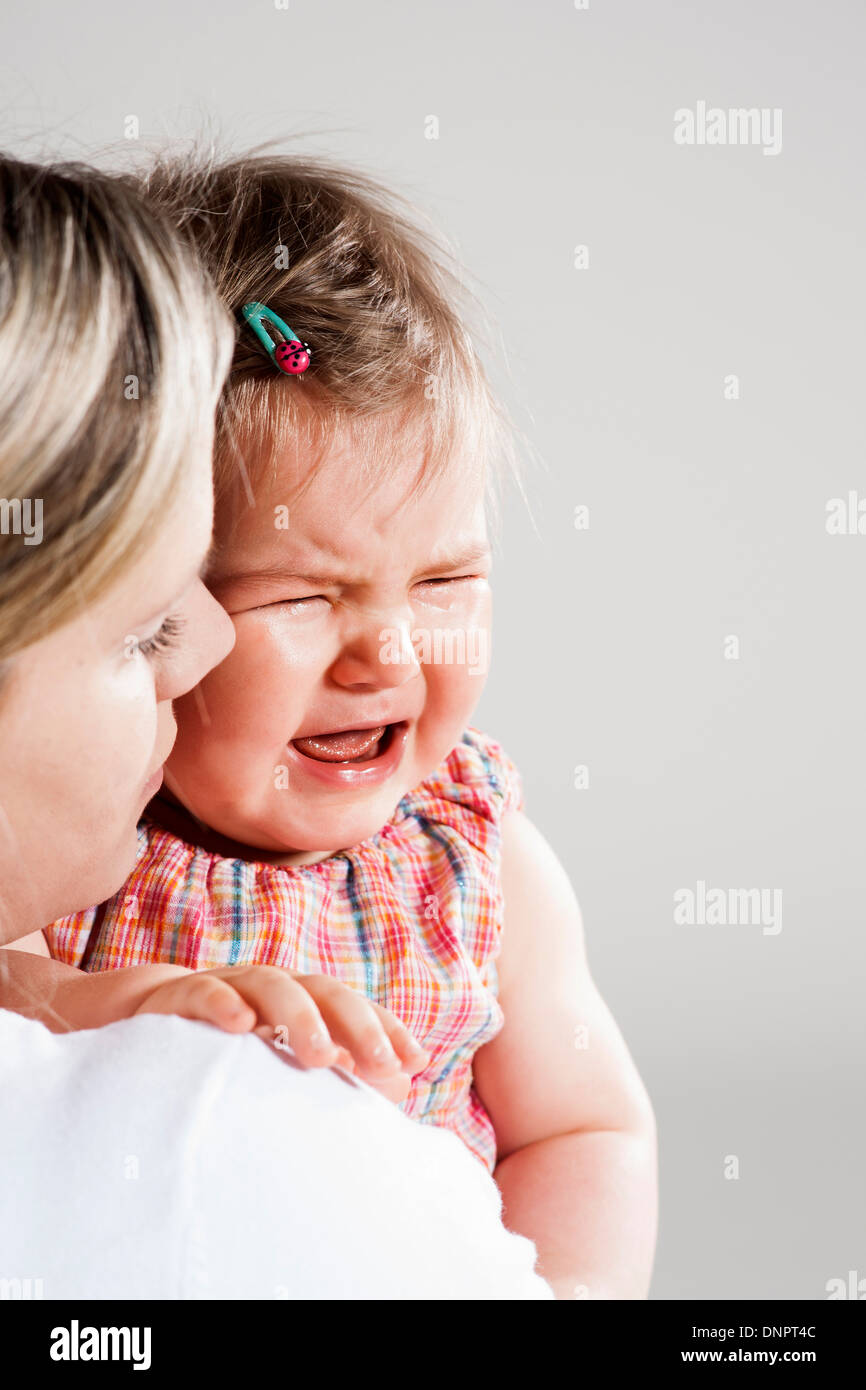 Portrait of Mother holding Crying Baby Girl, Studio Shot Stock Photo