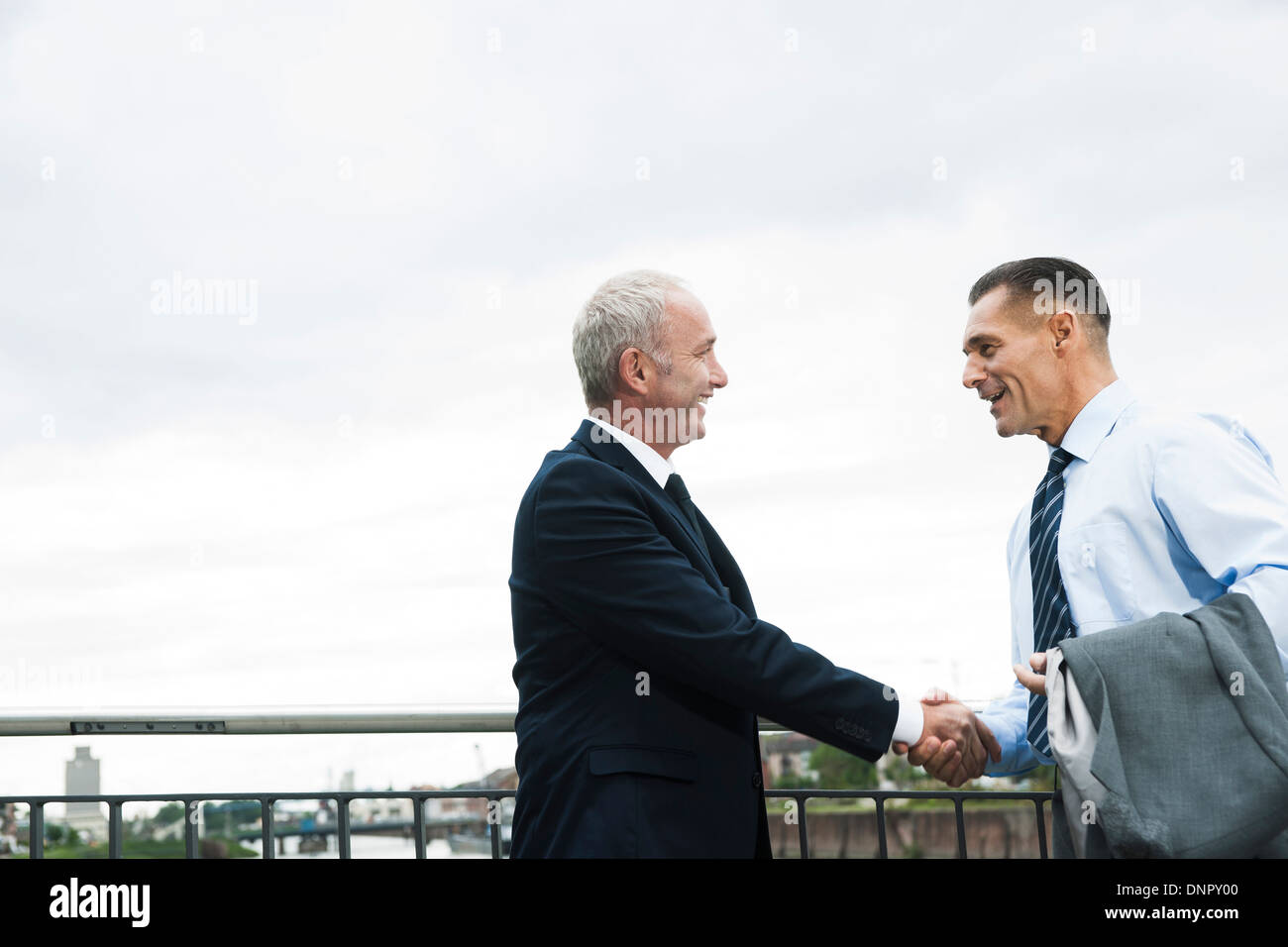 Mature businessmen standing by railing, shaking hands outdoors, Mannheim, Germany Stock Photo