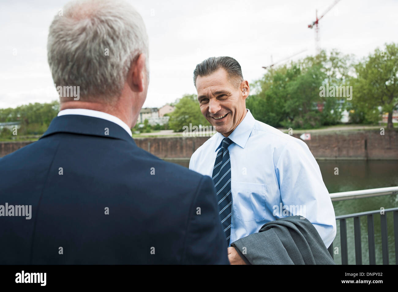 Mature businessmen standing by railing talking, Mannheim, Germany Stock Photo
