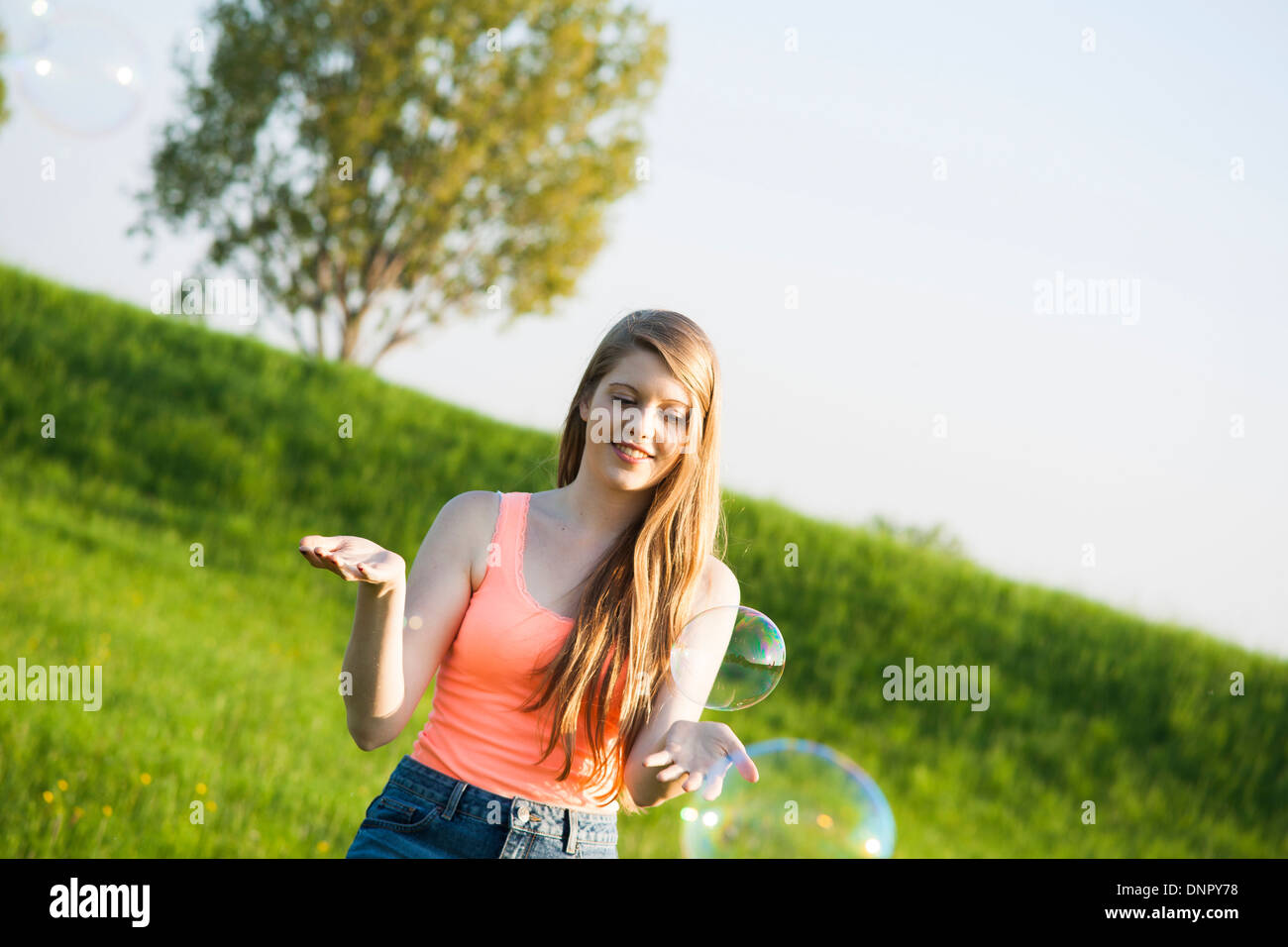Young woman standing in field playing with bubbles, Germany Stock Photo