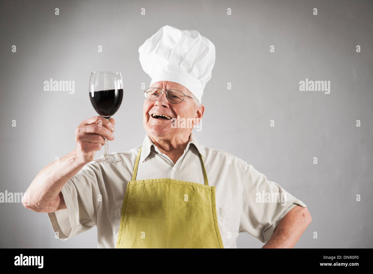 Senior Man with Red Wine wearing Apron and Chef's Hat, Studio Shot