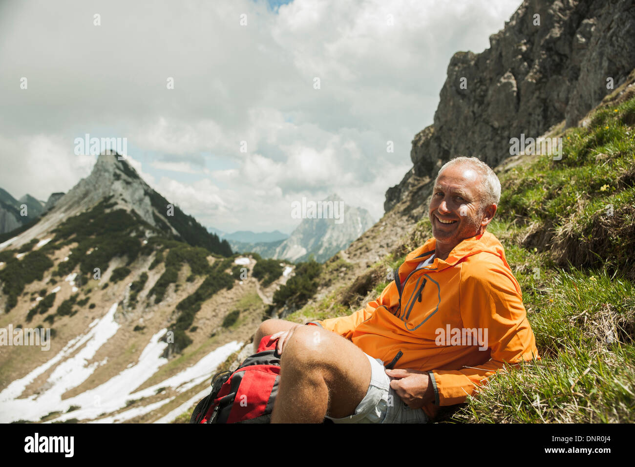 Portrait of mature man sitting on grass, hiking in mountains, Tannheim Valley, Austria Stock Photo
