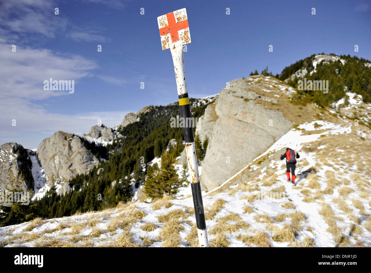 Red cross marking pole on a mountain in winter with hiker in background Stock Photo