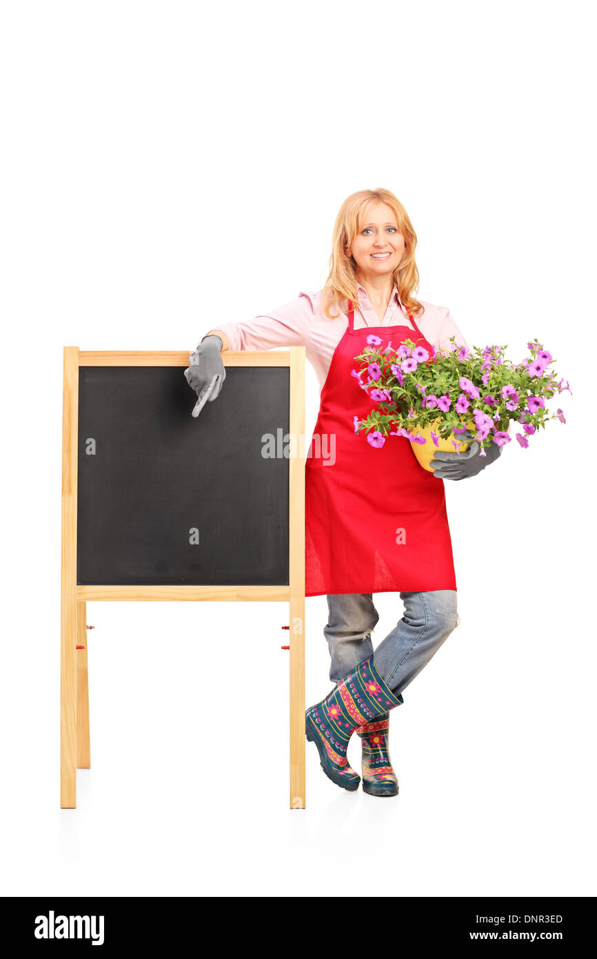 Full length portrait of female gardener standing next to black table and holding flowers Stock Photo