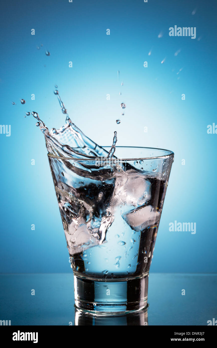 Ice cube splashing into a glassl of water. Blue background Stock Photo ...