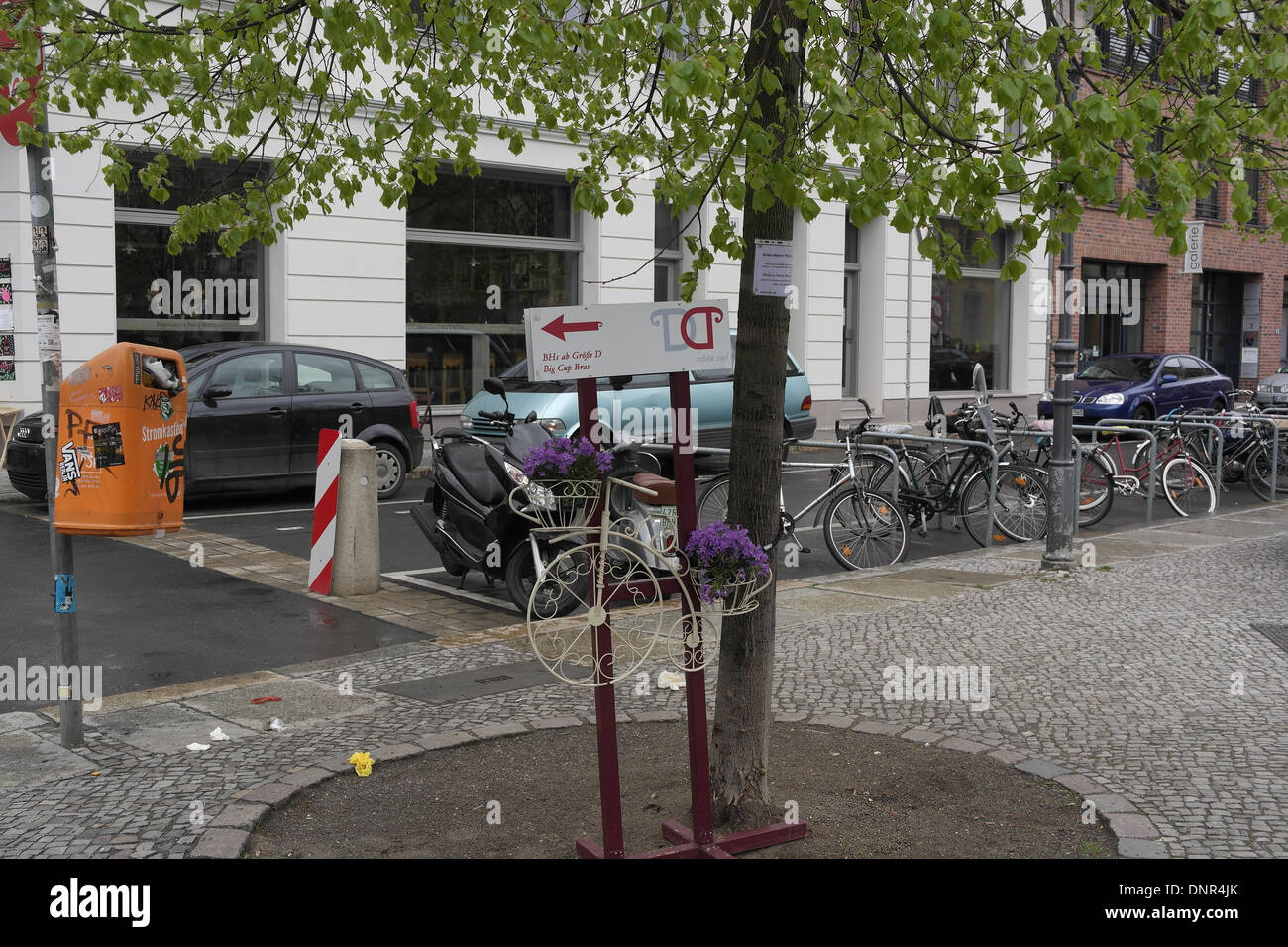 View chained bicycles, Mozzarella Bar windows, small Penny-Farthing with purple flowers by pavement tree, Joachimstrasse, Berlin Stock Photo