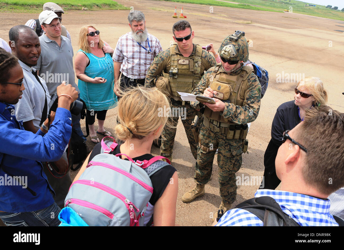 A US Marine from the Crisis Response team guides American citizens to an evacuation flight January 3, 2014 in Juba, South Sudan. The Marines evacuated more than 20 personnel from the U.S. Embassy as conflict escalates in South Sudan following a failed coup attempt. Stock Photo