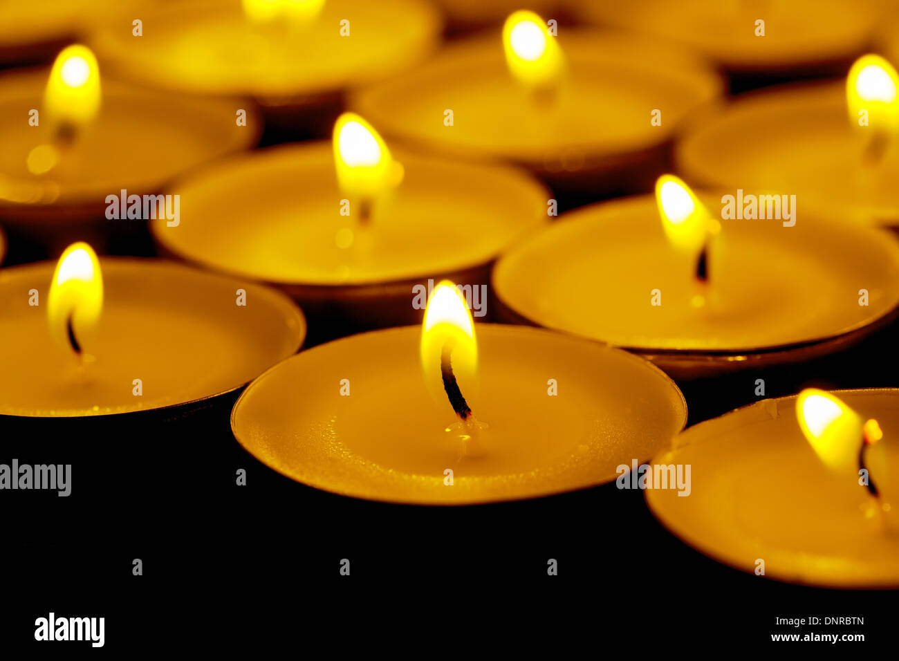 Tea lights candles with fire on dark background Stock Photo