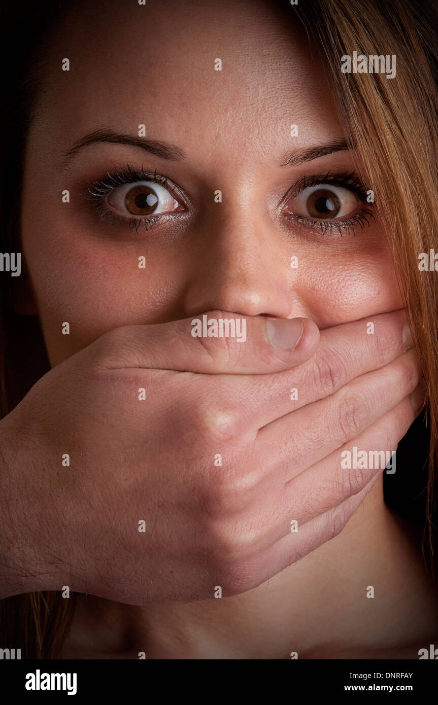 Closeup of a mans hand covering a womans mouth. Concept of domestic violence or kidnapping. Dark mood. Stock Photo