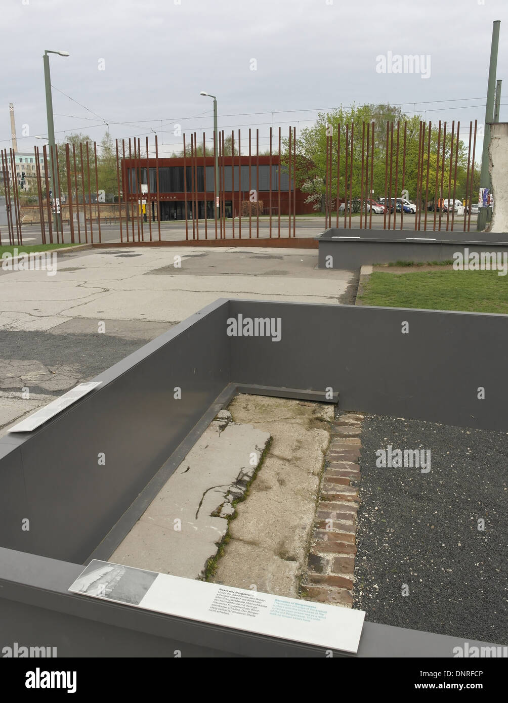 Grey sky view, to metal poles border wall, broken remains asphalt