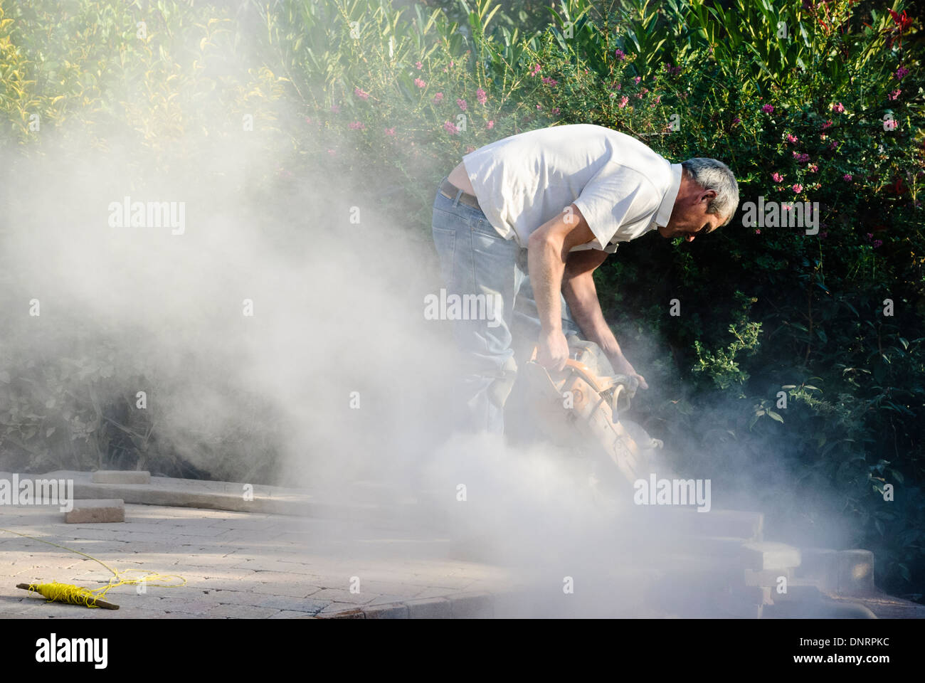 A builder uses an angle grinder to cut bricks while laying a patio Stock Photo