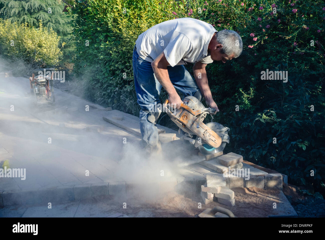 A builder uses an angle grinder to cut bricks while laying a patio Stock Photo