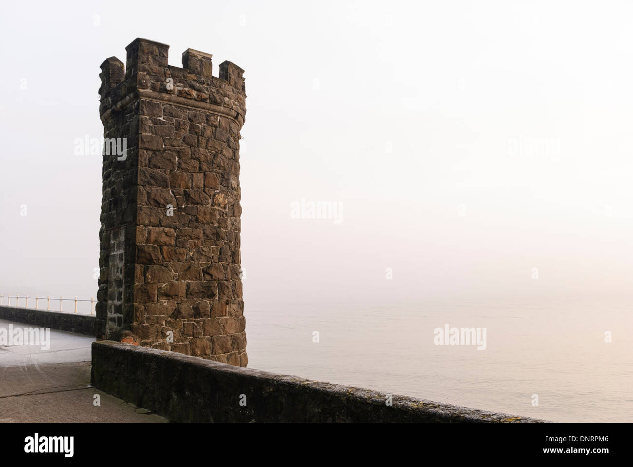 Stone castlated tower on a sea wall on a misty morning Stock Photo