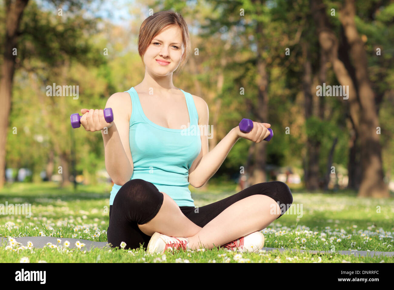 Female athlete exercising with dumbbells in a park Stock Photo