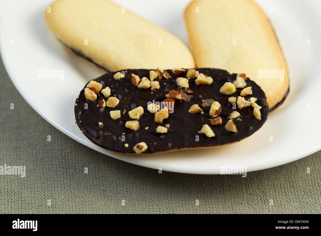 Horizontal photo of dark rich chocolate cookies and nuts on white plate with textured table cloth underneath Stock Photo