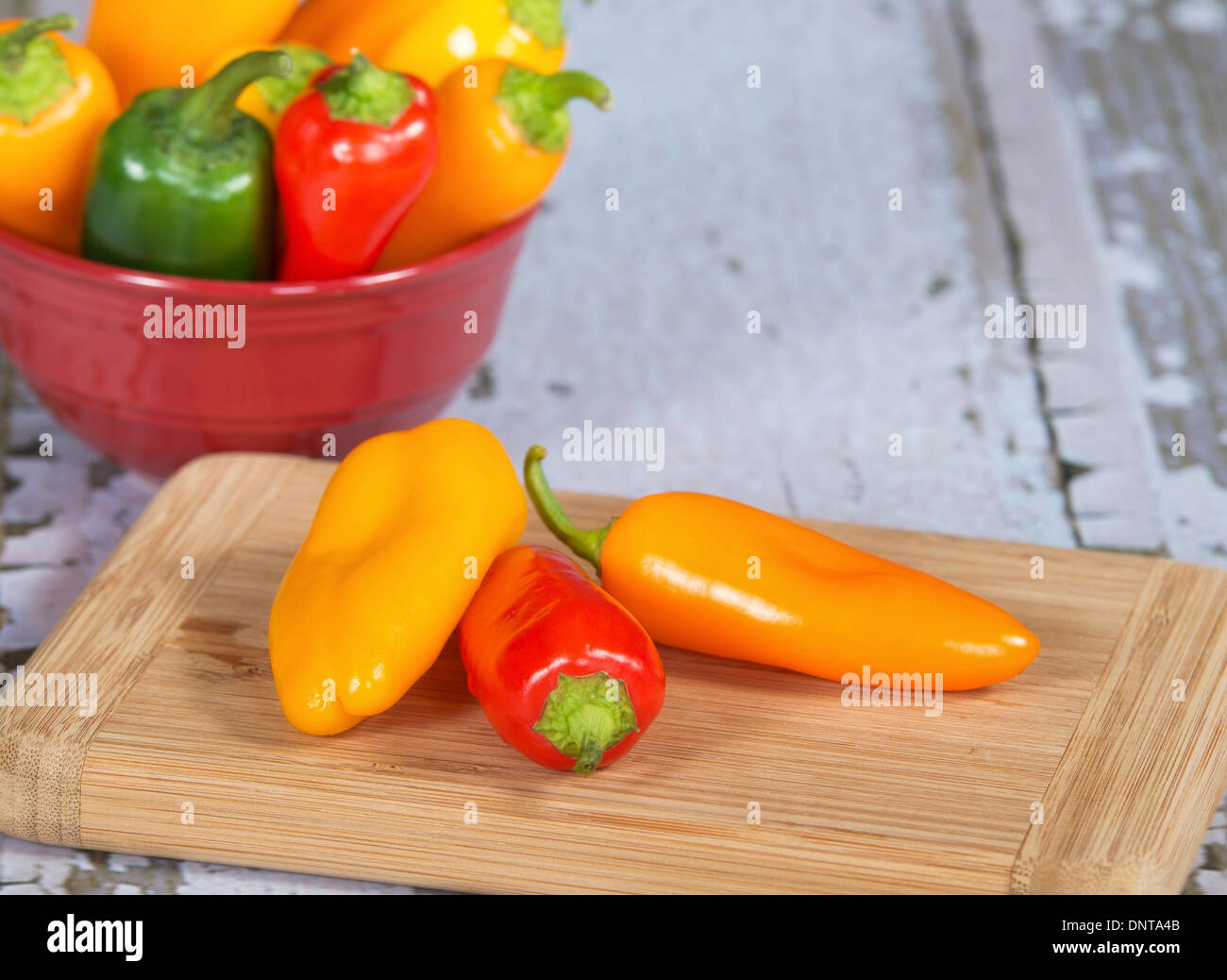 Colorful mini peppers on cutting board. A bowl of assorted peppers on the background. Stock Photo