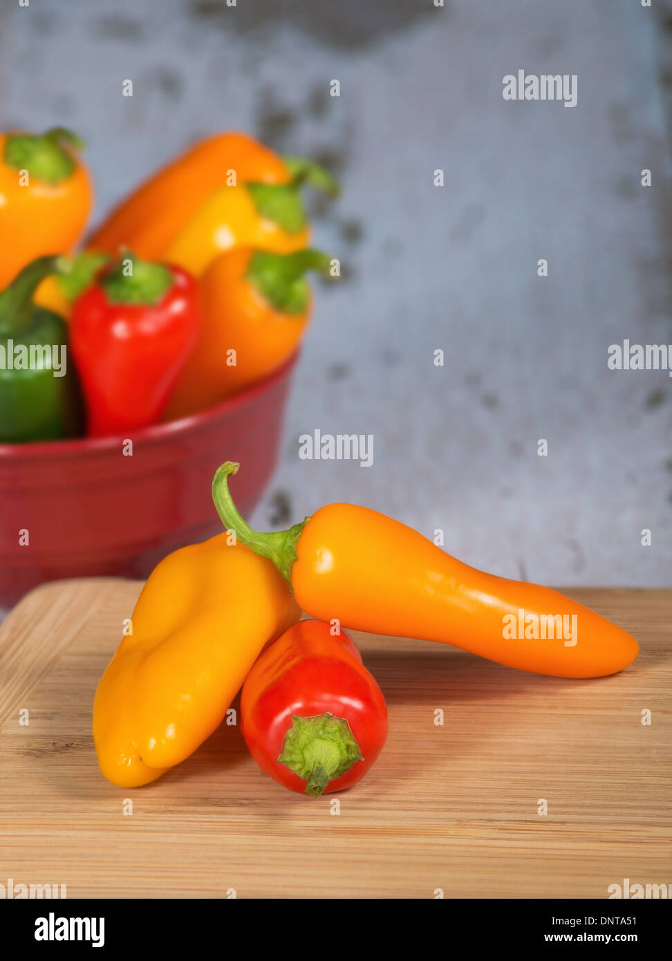 Colorful mini peppers on cutting board. A bowl of assorted peppers on the background with copy space. Stock Photo