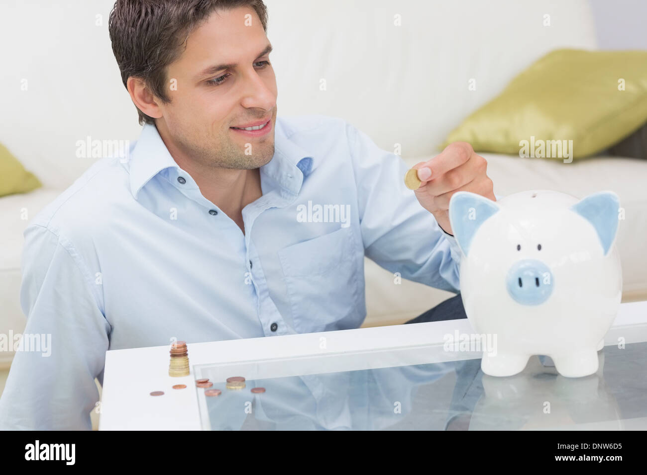 Casual man putting some coins into a piggy bank in living room Stock ...