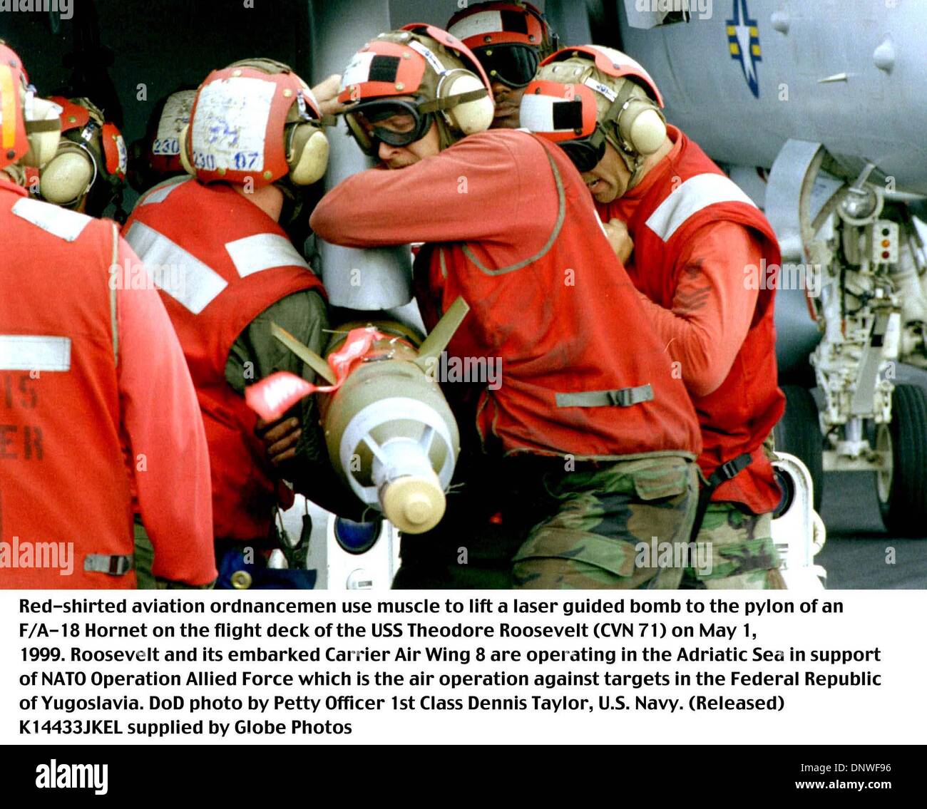 May 1, 1999 - Adriatic Sea - K14433JKEL     05/01/99.990501-N-6119T-003..Red-shirted aviation ordnancemen use muscle to lift a laser guided bomb to the pylon of an F/A-18 Hornet on the flight deck of the USS Theodore Roosevelt (CVN 71) on May 1, 1999.  Roosevelt and its embarked Carrier Air Wing 8 are operating in the Adriatic Sea is support of Operation Allied Force which is the a Stock Photo