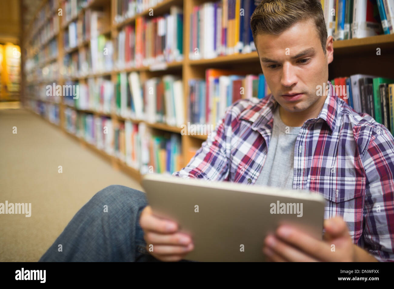 Serious young student sitting on library floor using tablet Stock Photo